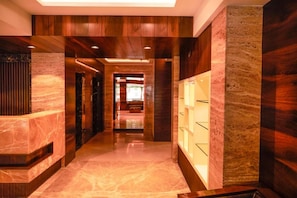 A hallway with a marble floor, wooden paneling, and a glass display case. - Pravasa Hotel Indore (Indore)