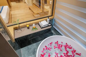 A bathroom with a bathtub filled with rose petals, a mirror, a shelf with toiletries, and a plant. - Pravasa Hotel Indore (Indore)