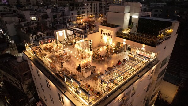 A rooftop bar with multiple seating areas, a bar counter, and a large illuminated sign.