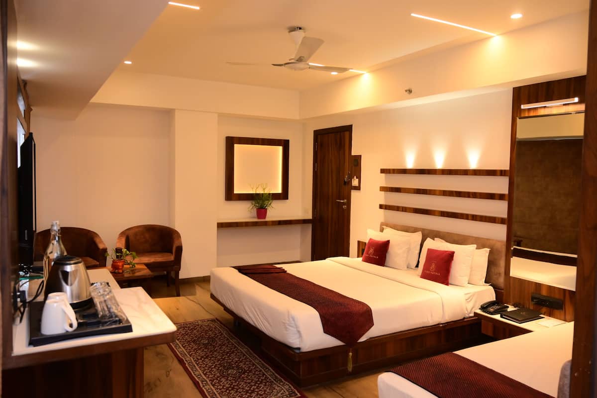 A modern hotel room with a large bed, a desk with a coffee maker, a chair, a small table with a plant, and a mirror on the wall.