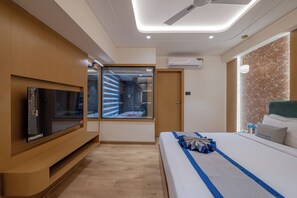 A modern hotel room with a flat-screen TV, a large window with a view, a ceiling fan, and a bed with a blue-striped bedspread. - Pravasa Hotel Indore (Indore)