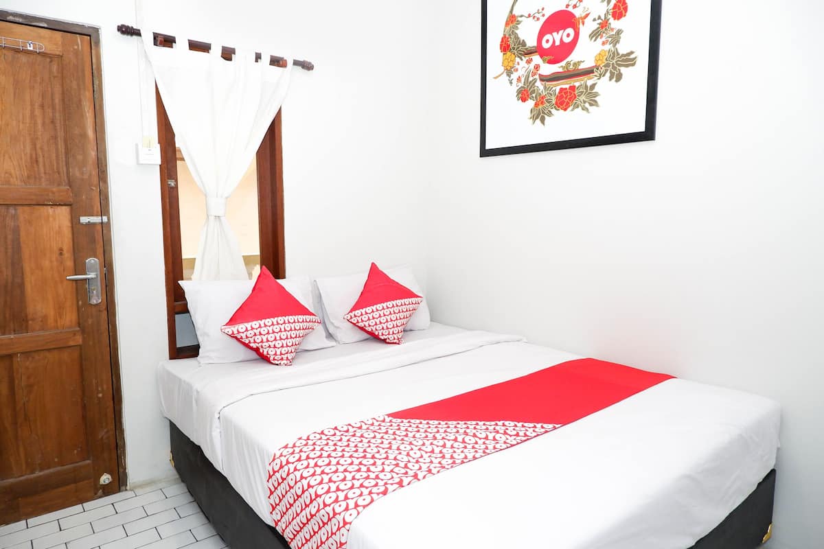 Ein ordentlich bezogenes Bett mit einer rot-weißen Tagesdecke, eine Holztür und ein gerahmtes Bild an der Wand.