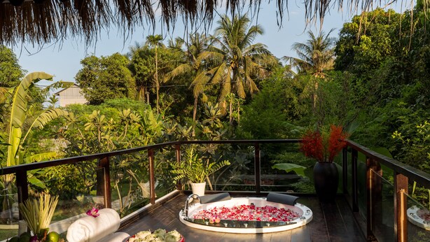 A spa area with a hot tub surrounded by lush greenery, a wooden deck, and a glass railing. - Sampeah Retreat Villa (Siem Reap)