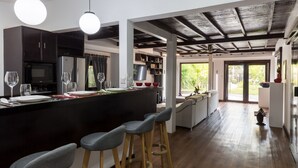 A modern kitchen with a central island, bar stools, and a dining area with a view of the outdoors. - Sampeah Retreat Villa (Siem Reap)
