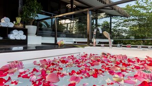 A modern hotel interior with a glass-enclosed pool area covered in rose petals, a thatched roof, and a view of lush greenery outside. - Sampeah Retreat Villa (Siem Reap)