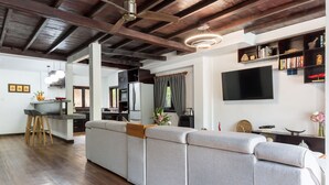 A modern living room with a large grey sectional sofa, wooden flooring, a ceiling fan, and a flat-screen TV mounted on the wall. - Sampeah Retreat Villa (Siem Reap)