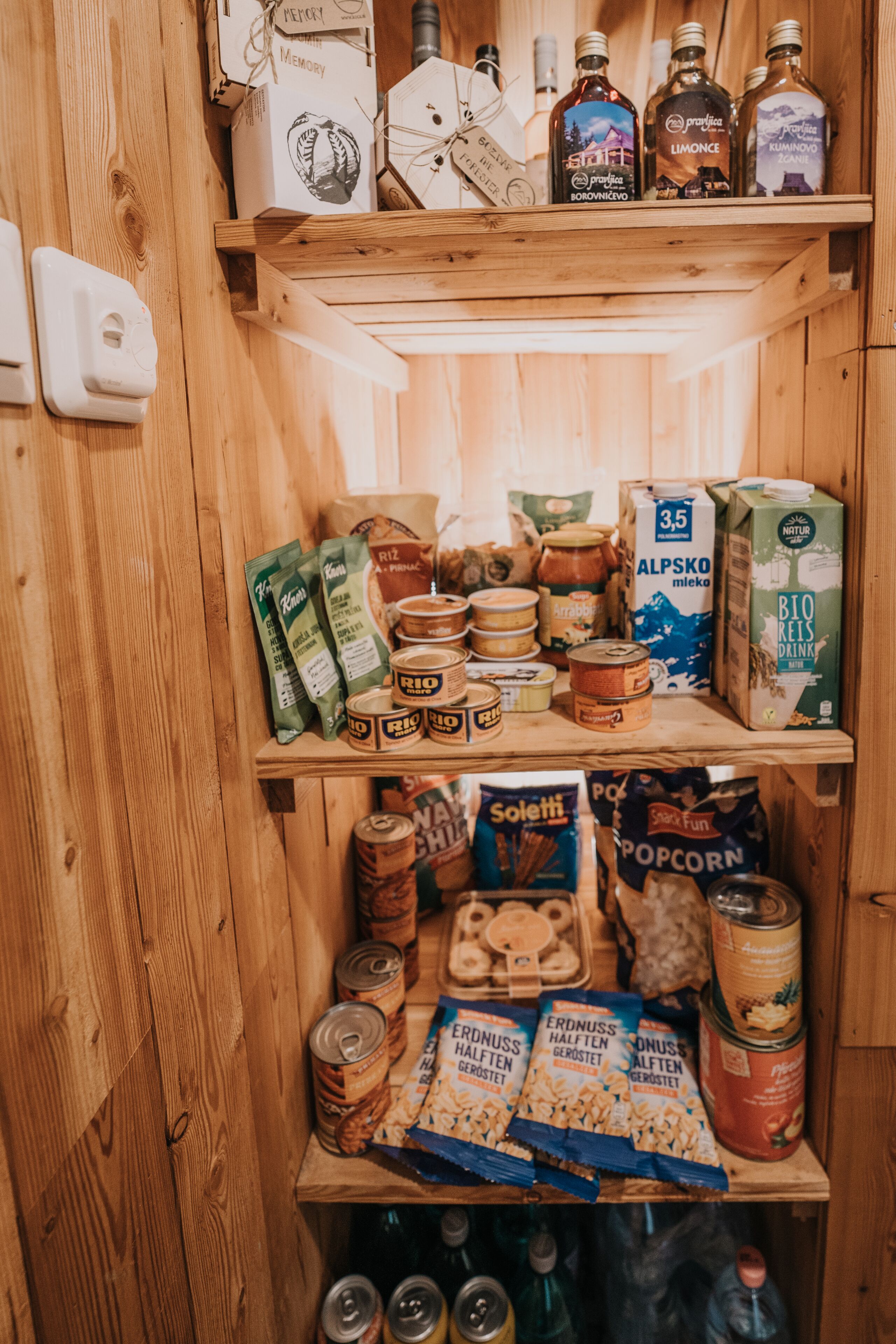 A wooden pantry with shelves stocked with food items, including jars, boxes, and canned goods.
