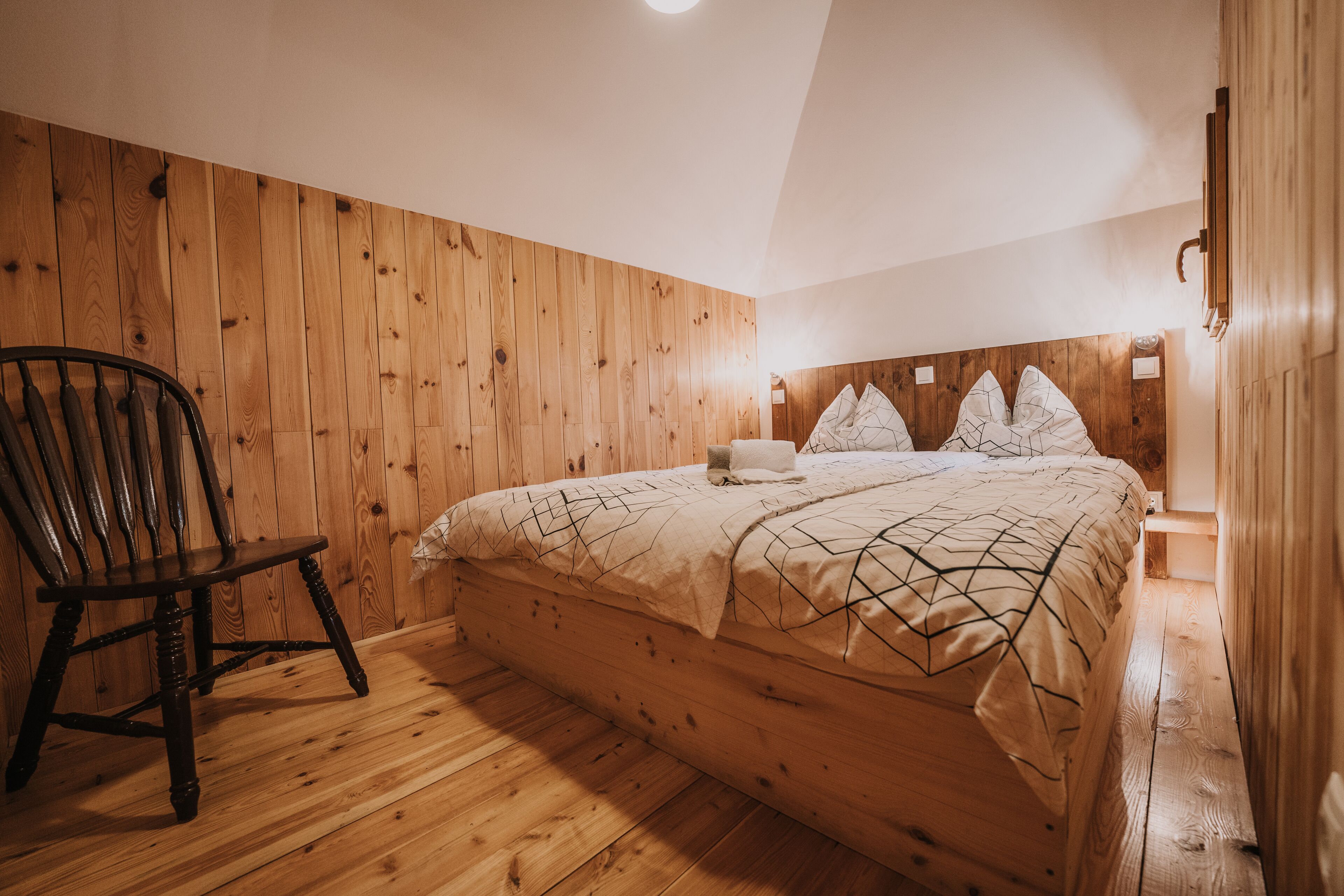 Ein Schlafzimmer mit Holzwänden, einem Bett, einem Sessel und einem Nachttisch.