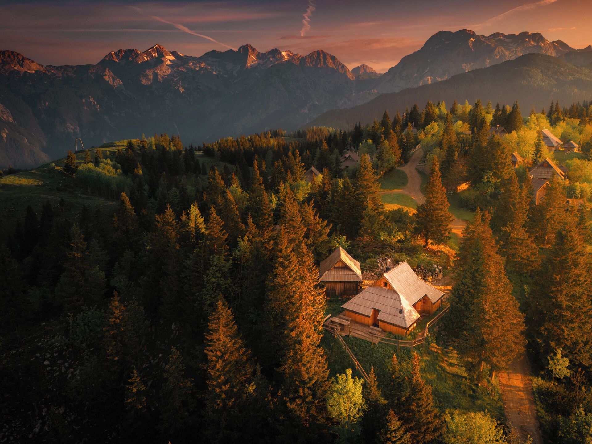 A mountainous landscape with a small cluster of wooden cabins surrounded by dense forest.