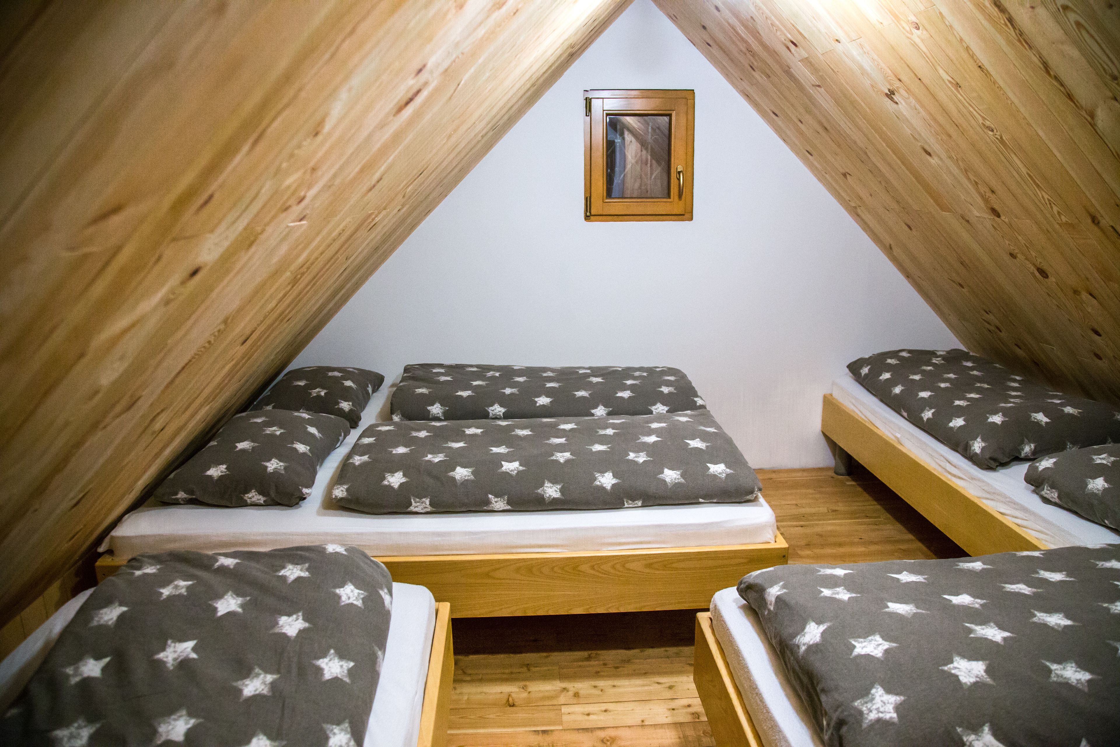Une petite chambre mansardée de forme triangulaire, équipée de trois lits, chacun avec une literie ornée de motifs en forme d’étoiles.