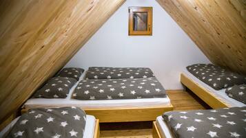 Une petite chambre mansardée de forme triangulaire, équipée de trois lits, chacun avec une literie ornée de motifs en forme d’étoiles.