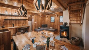 Un acogedor interior de cabaña con una mesa de comedor de madera, un sofá, una chimenea y una lámpara colgante.