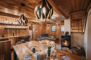 Un acogedor interior de cabaña con una mesa de comedor de madera, un sofá, una chimenea y una lámpara colgante.