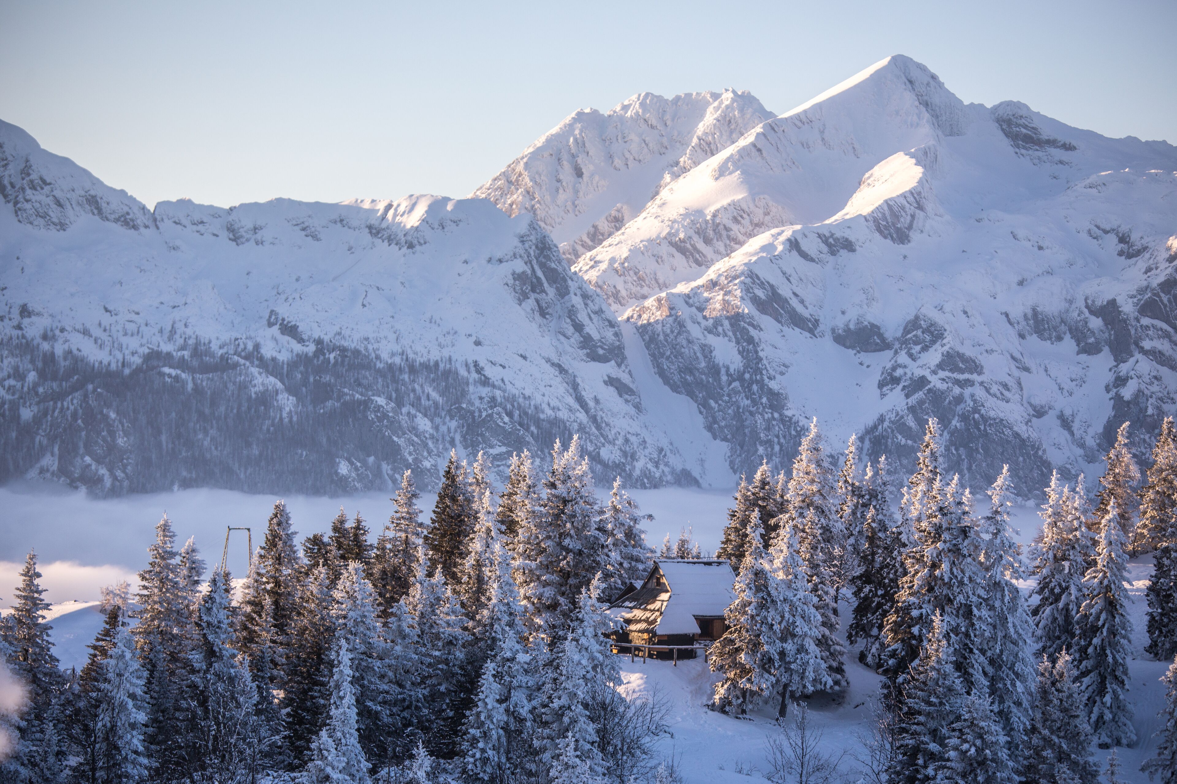 Un paisaje montañoso cubierto de nieve con una cabaña ubicada entre árboles.