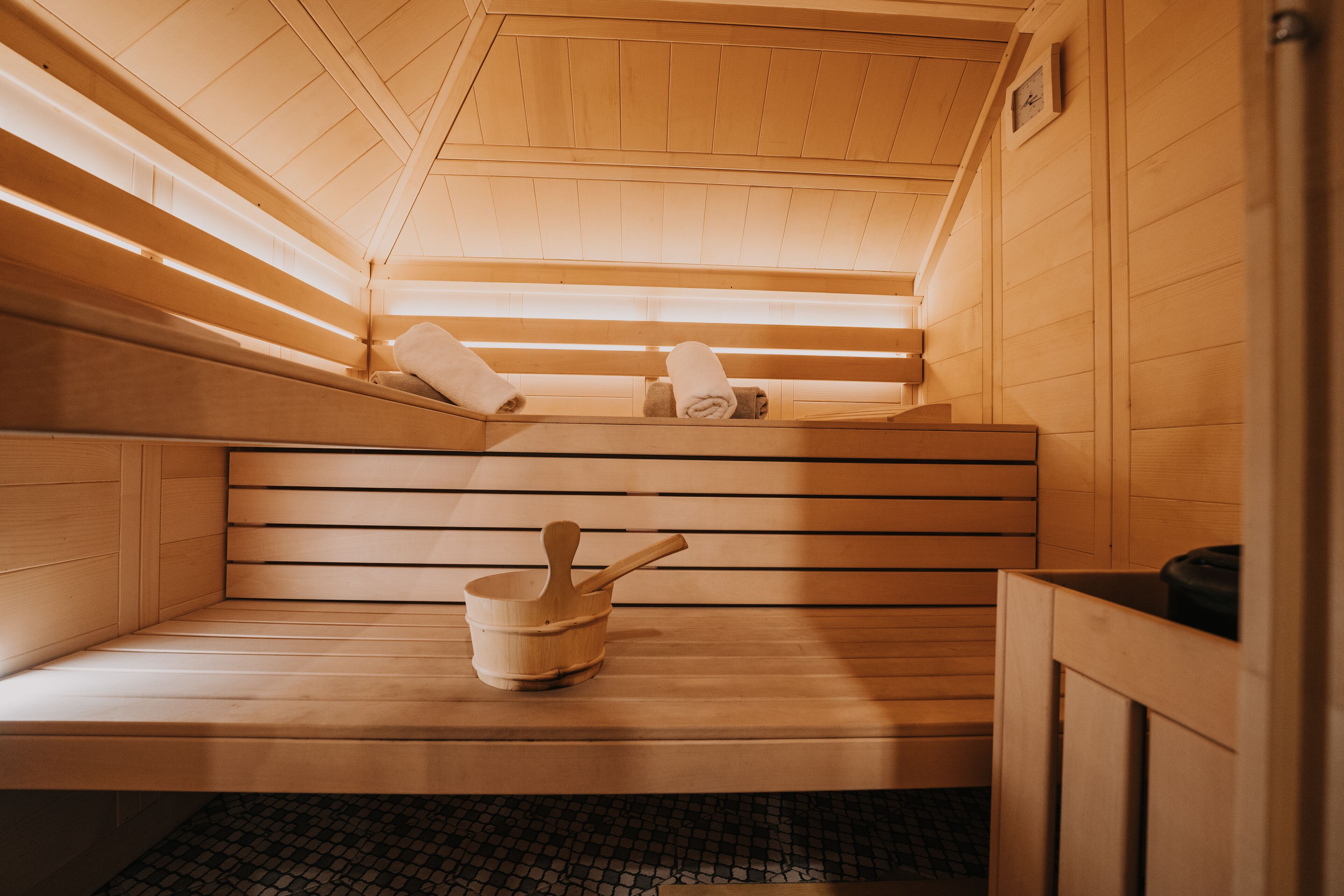 A sauna with wooden benches, a wooden bucket, and towels.
