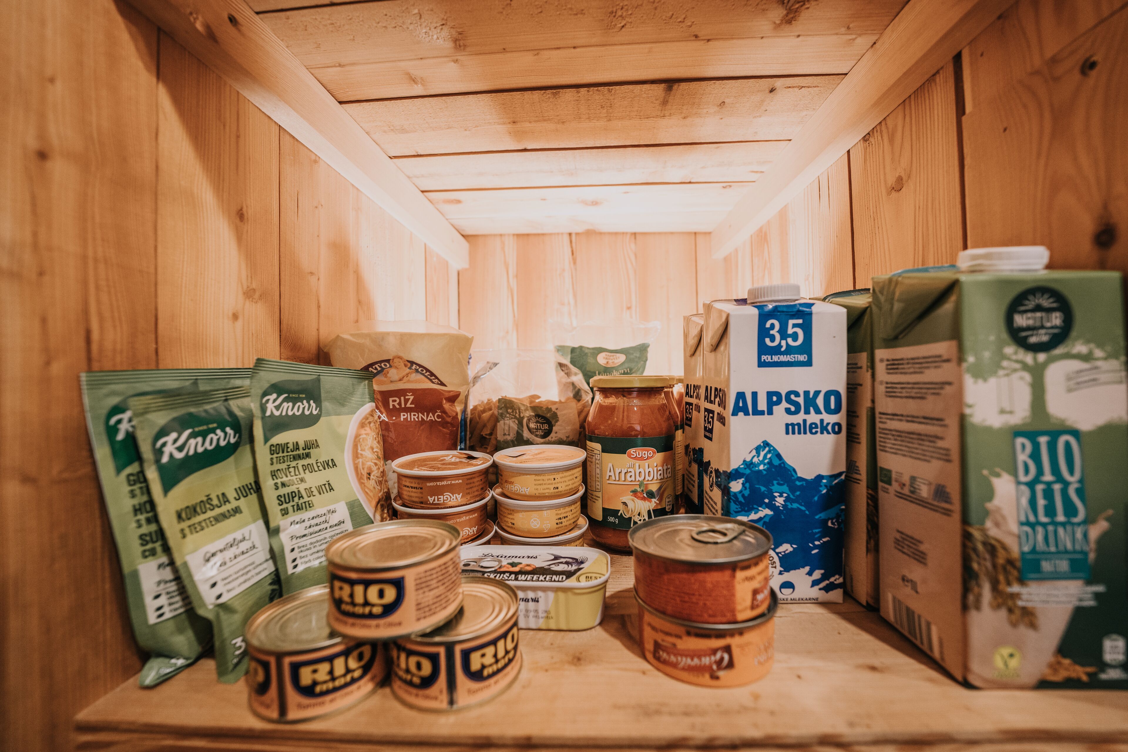 A wooden cabinet with various food items including canned goods, bags of rice, and a carton of milk.