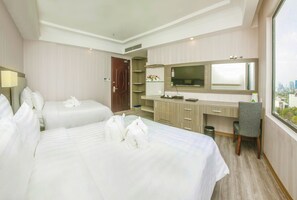 A hotel room with two beds, a desk, a chair, a TV, and a window with a city view. - Golden Rose Hotel Danang (Da Nang)