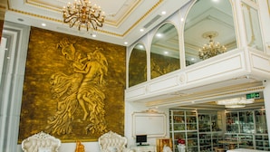 Un lobby imponente con murales dorados ornamentados, muebles blancos elegantes y una araña.