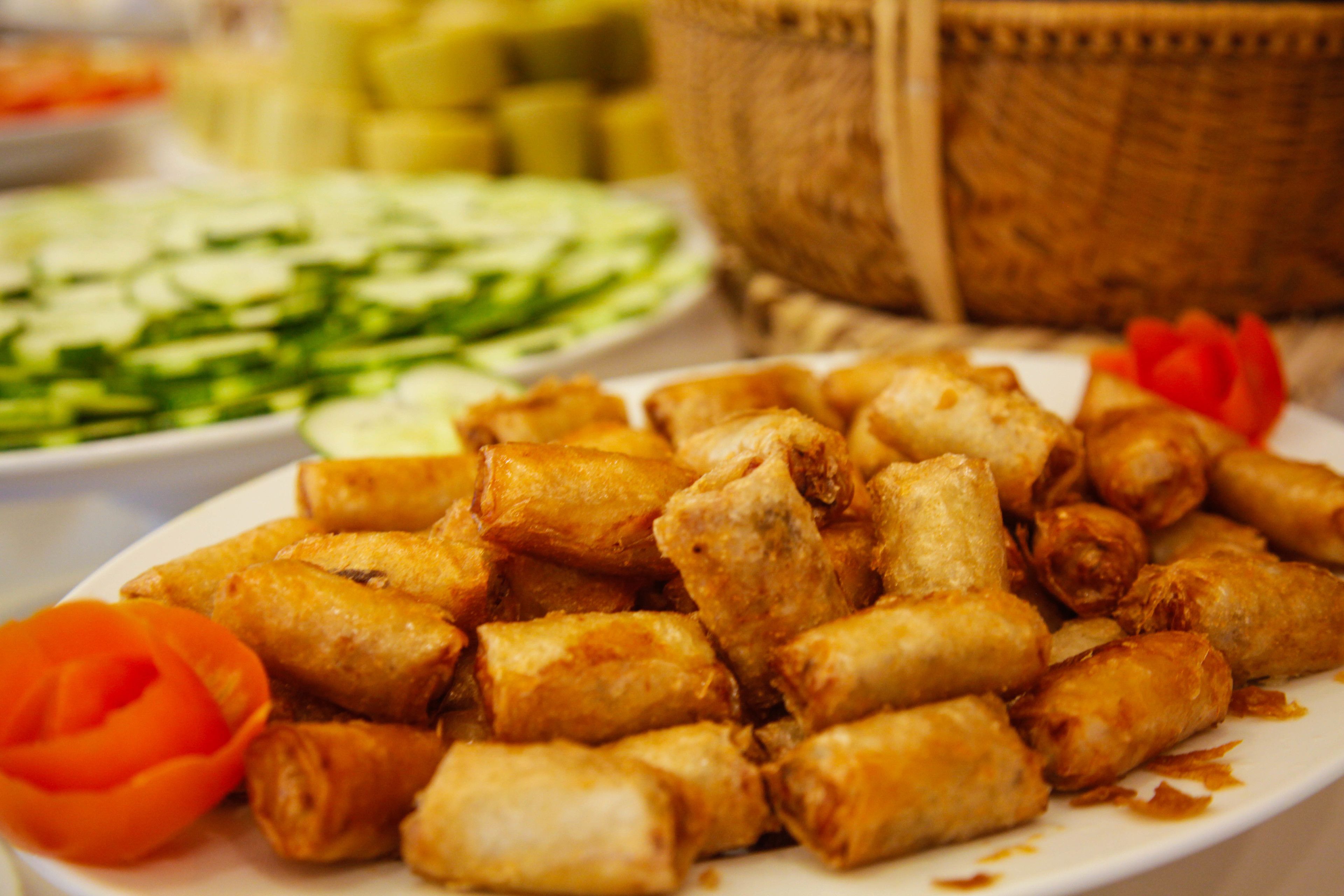 A plate of fried spring rolls with a side of sliced cucumbers and a decorative flower.