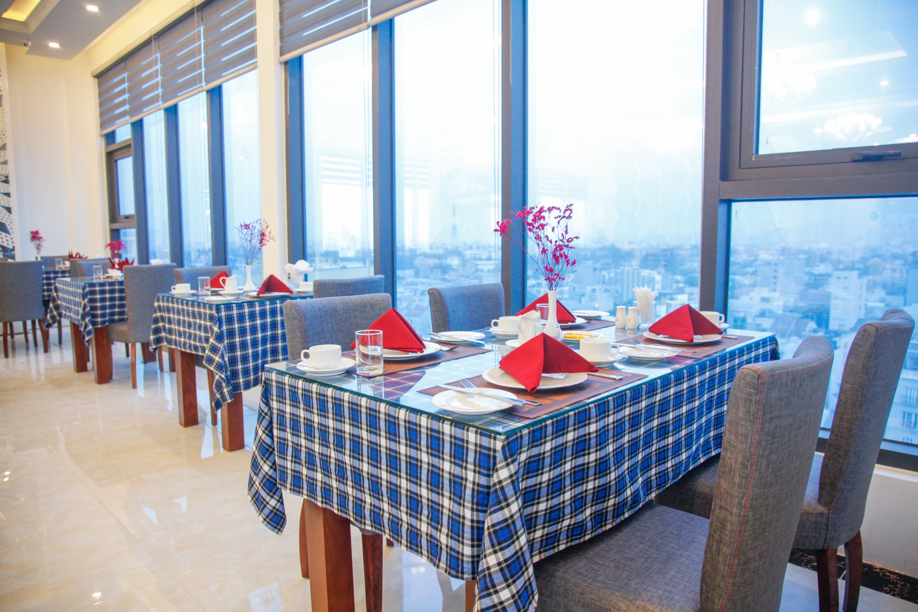 Un restaurant avec des tables dressées, de grandes fenêtres et une vue sur la ville.