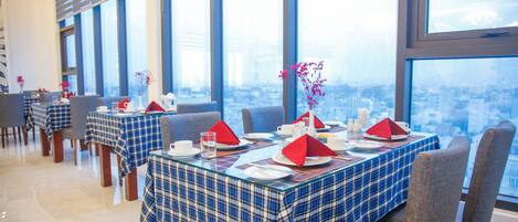 Un restaurant avec des tables dressées, de grandes fenêtres et une vue sur la ville.