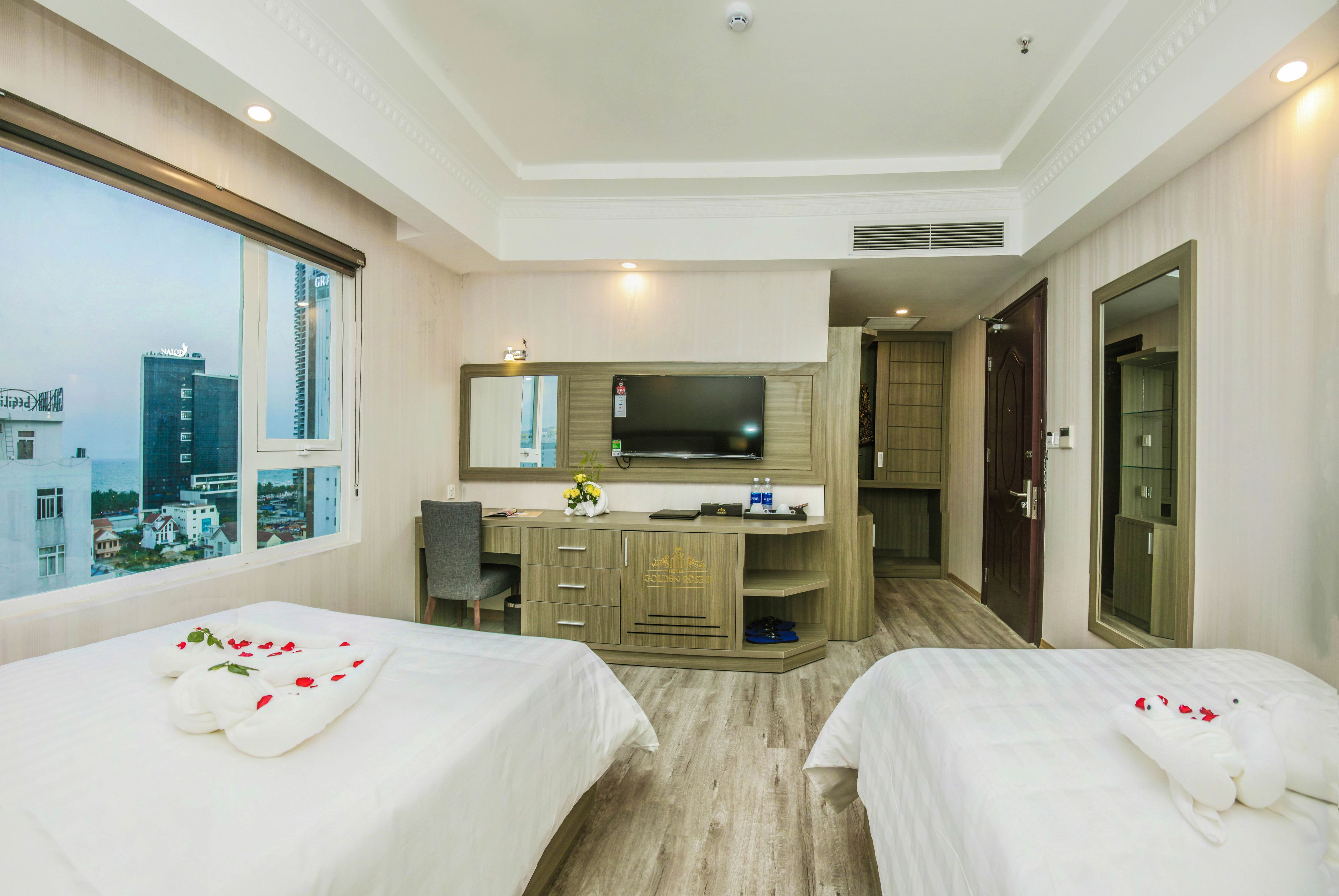 Habitación de hotel con dos camas, un escritorio, televisión y un amplio ventanal con vistas a la ciudad.
