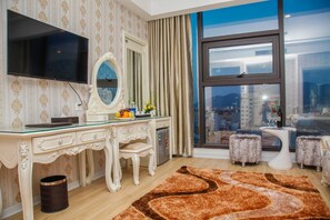 A well-appointed bedroom with a large flat-screen TV, a vanity with a mirror, a dresser, and a large window offering a city view. - Golden Rose Hotel Danang (Da Nang)