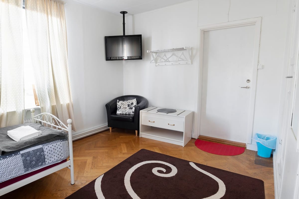 A bedroom with a bed, a chair, a nightstand, a TV, and a door.