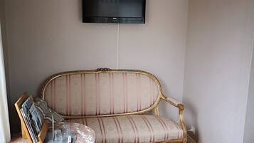 A room with a sofa, a small table with magazines and glasses, a television on the wall, and a bed with a blanket.