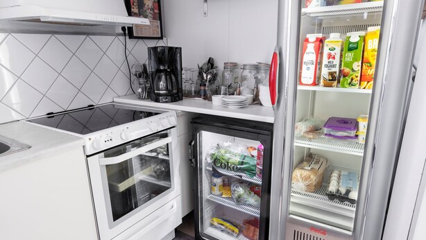 A compact kitchen with a built-in oven, a coffee maker, and a mini-fridge stocked with beverages and snacks. - Värdshuset i Motala (Motala)