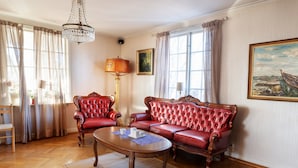 A room with a red leather sofa, a wooden coffee table, a chandelier, and a painting on the wall. - Värdshuset i Motala (Motala)
