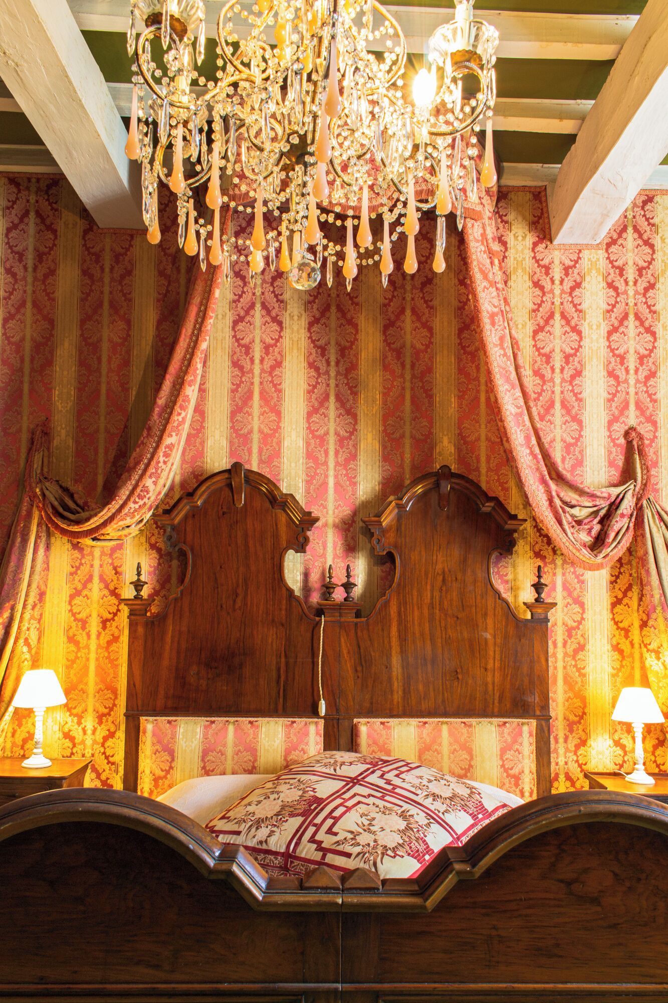 A room with a wooden headboard, ornate curtains, and a chandelier.