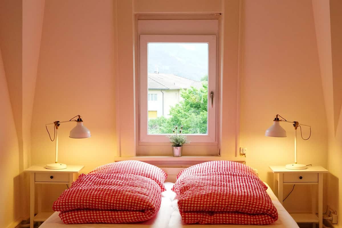 A bedroom with a bed, two bedside tables, a window, and a hanging light fixture.
