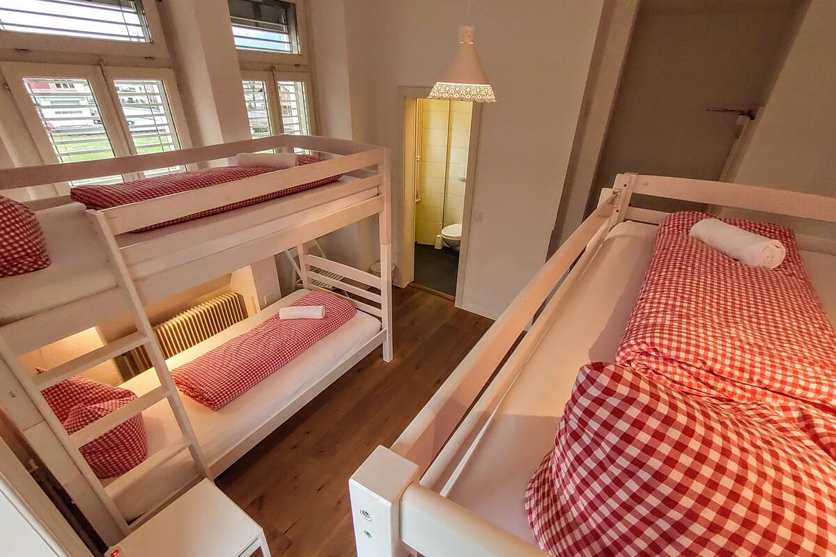 A bunk bed room with a window, a desk, and a lamp.