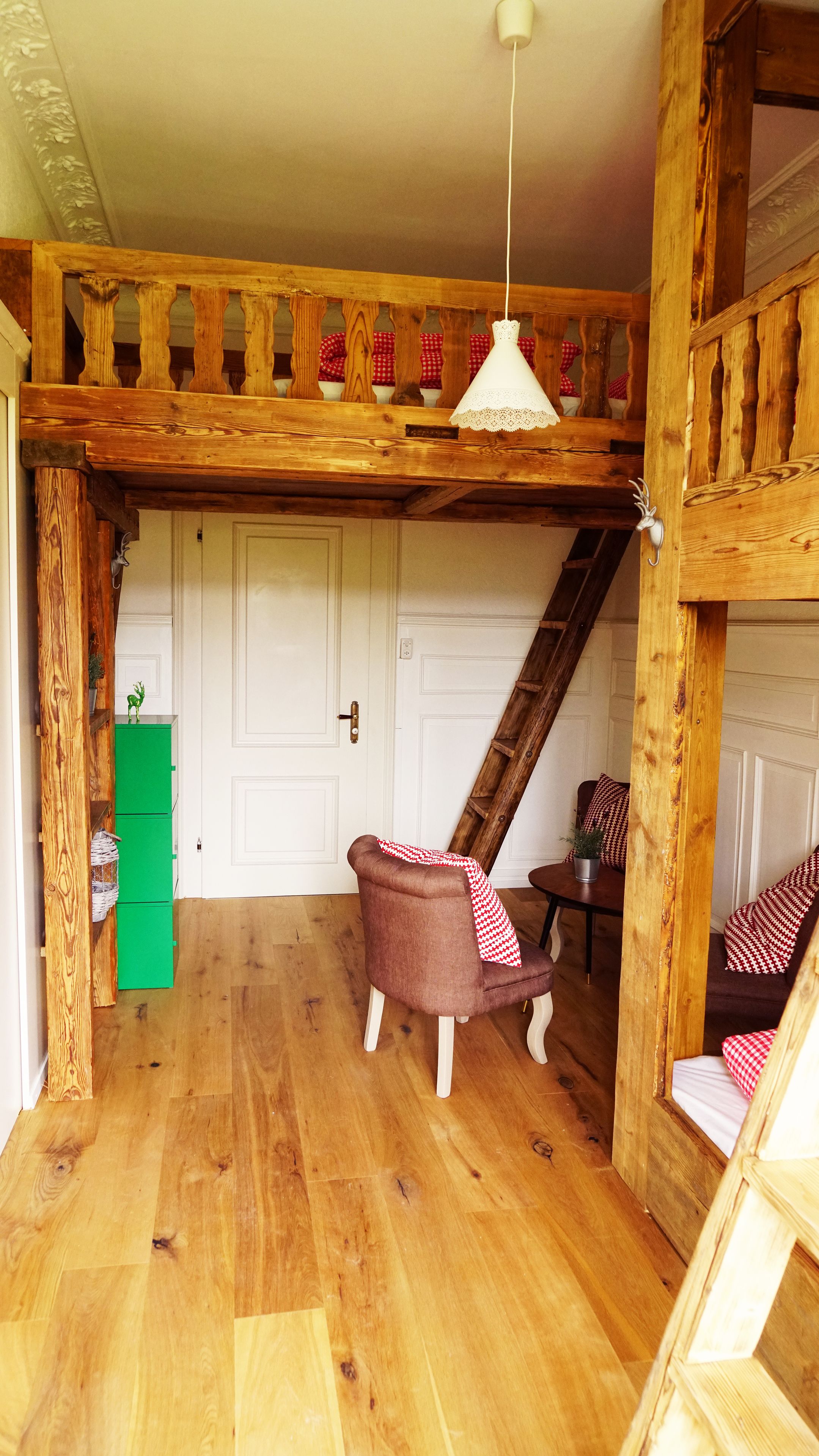 Un dormitorio rústico con cama de altillo, un refrigerador verde, una silla de madera y una mesita.