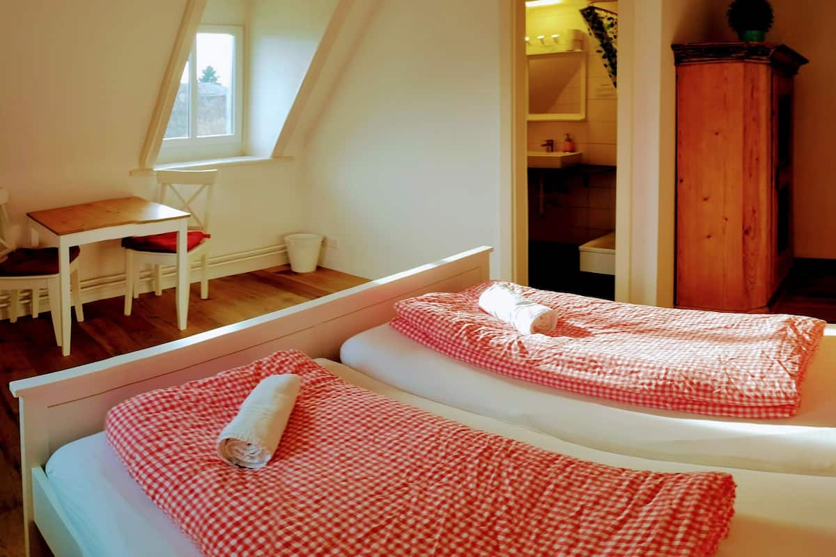 A bedroom with a bed, a small table, and a chair. There is a window and a wooden cabinet.