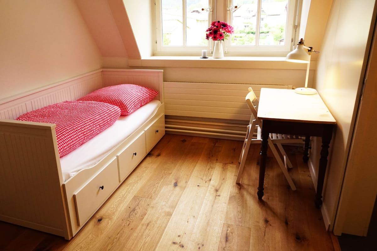 A small, cozy bedroom with a single bed, a desk, and a window with a view.