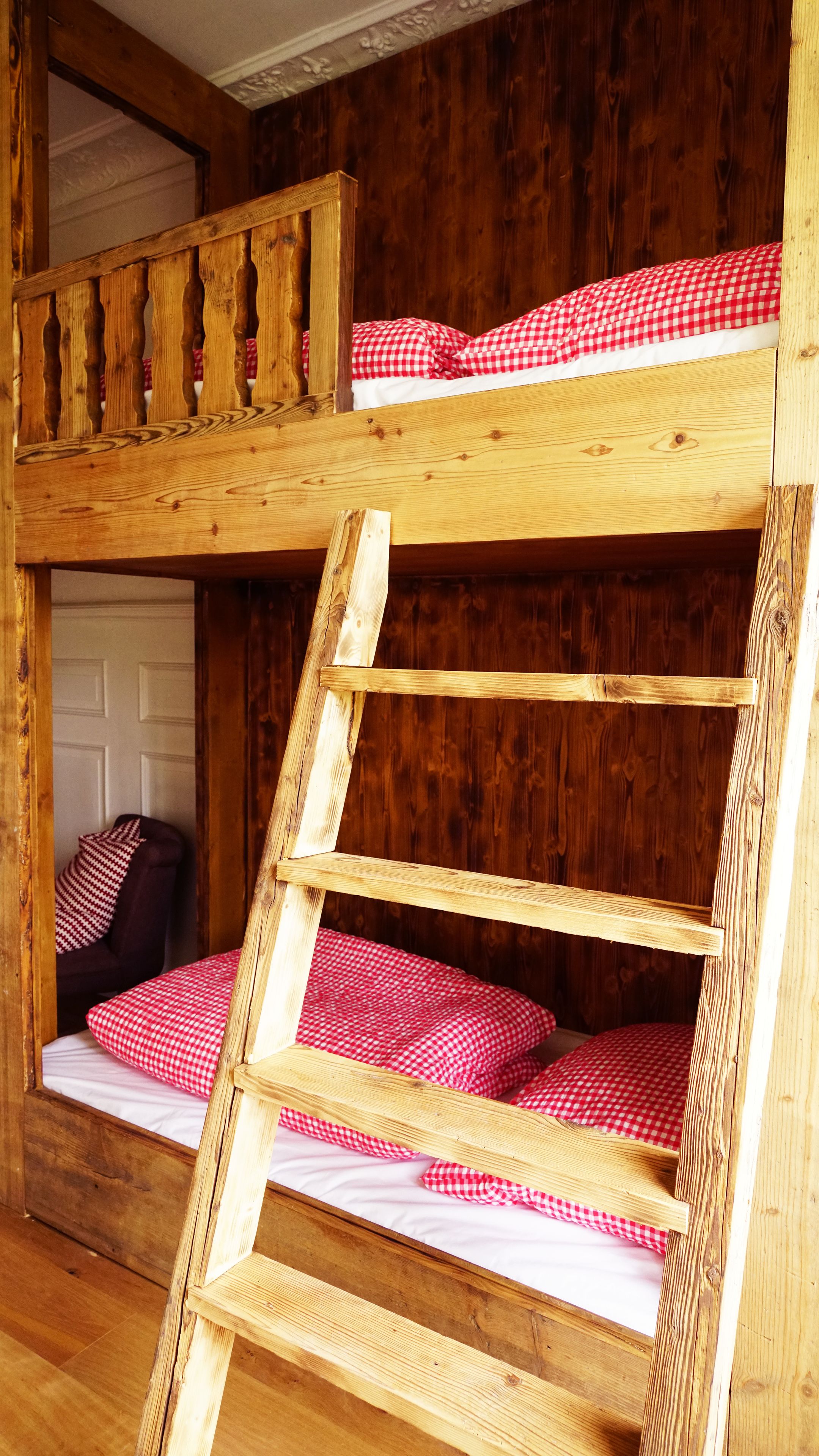 Ein Etagenbett mit Holzleiter, roter Karo-Bettwäsche und einer Holzwand.