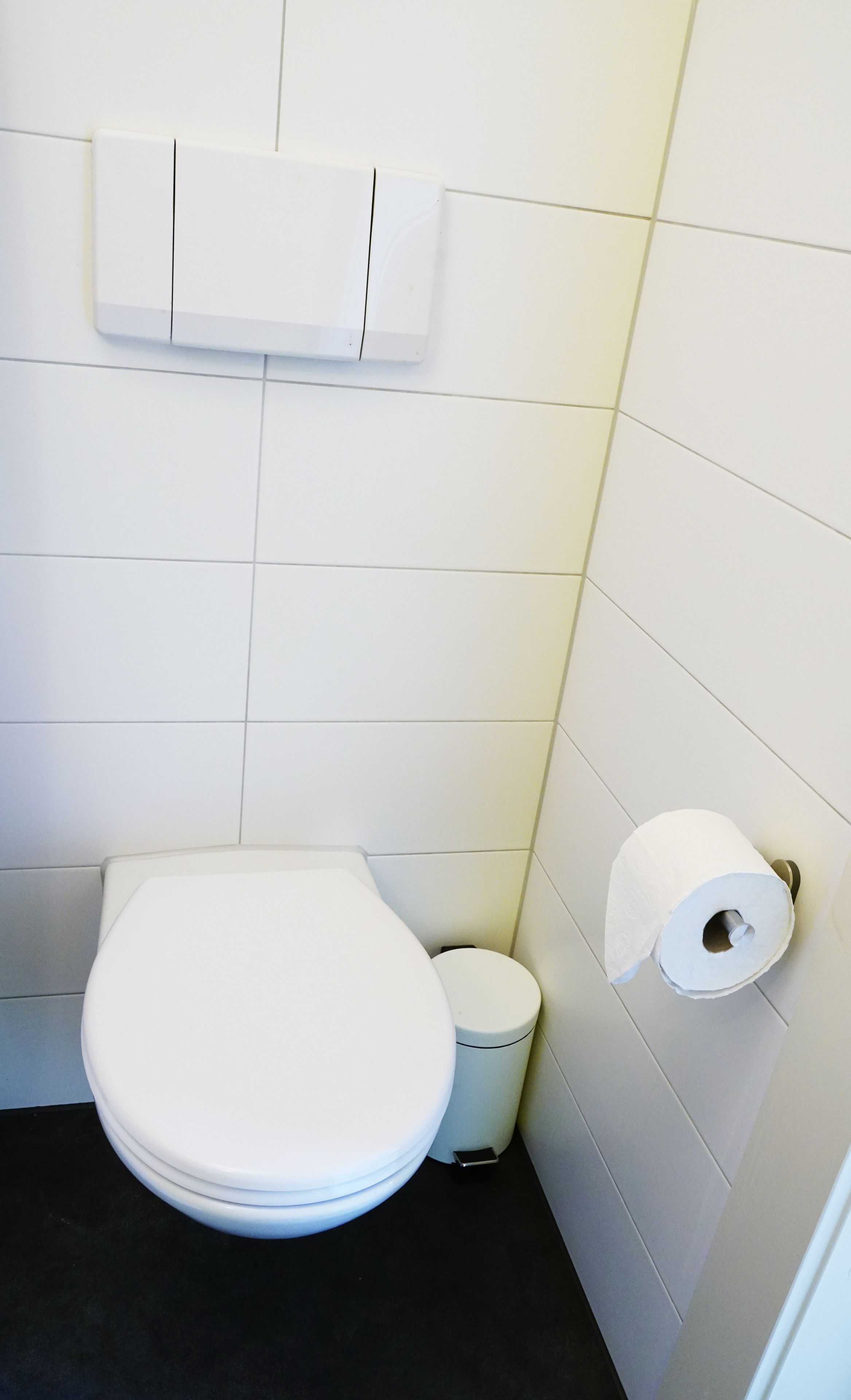 Ein kleines, sauberes Badezimmer mit einer weißen Toilette, einer kleinen Mülltonne und einem Toilettenpapierhalter an der Wand.