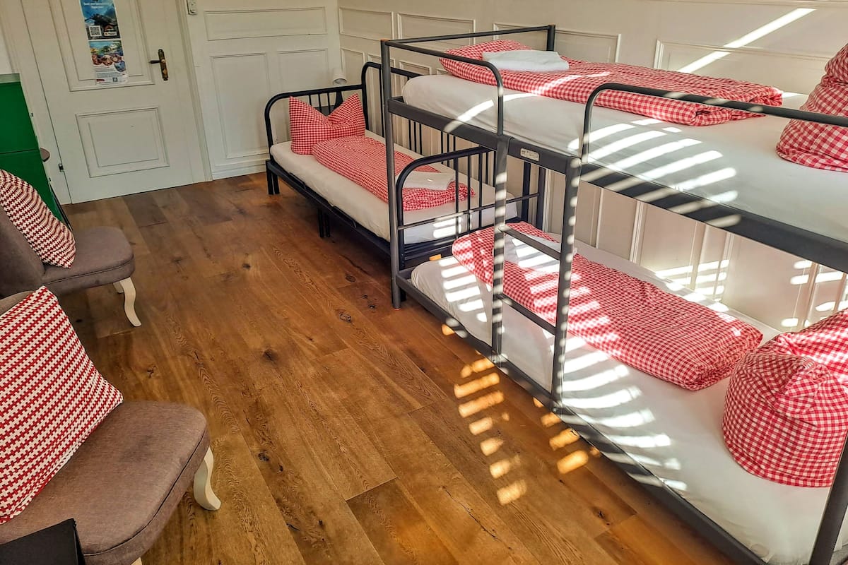 A bunk bed room with checkered bedding, a wooden floor, and a green chair.