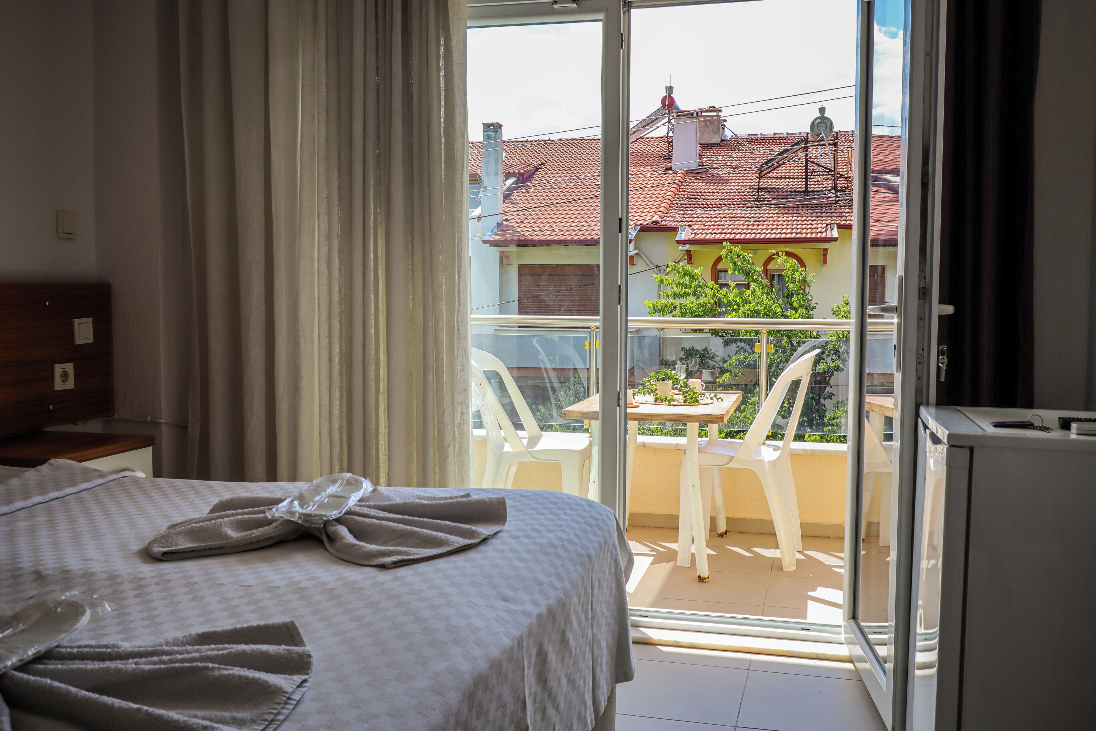 A hotel room with a bed, a balcony with a table and chairs, and a view of the neighborhood.
