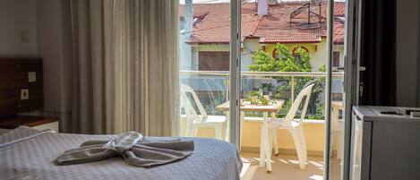 A hotel room with a bed, a balcony with a table and chairs, and a view of the neighborhood.