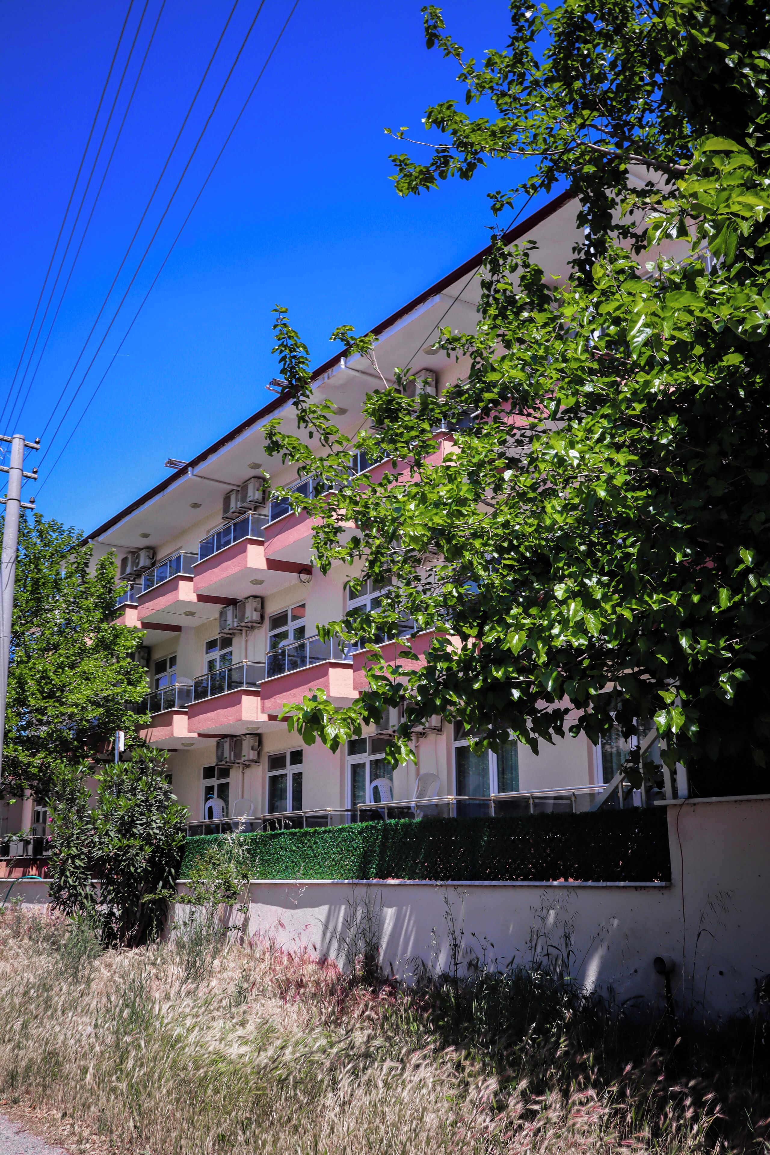 A multi-story building with balconies, surrounded by greenery and a clear blue sky.