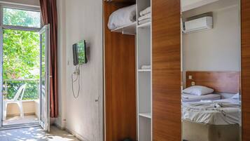 Une chambre d’hôtel avec un balcon, une armoire en bois, un lit avec un matelas et des oreillers blancs, et un climatiseur fixé au mur.