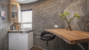 A compact kitchen with a built-in refrigerator, a wooden bar table, a black chair, and a small potted plant. - Klettar Tower Iceland (Selfoss)