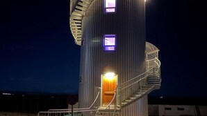 A cylindrical tower with a spiral staircase, illuminated windows, and a metal railing. - Klettar Tower Iceland (Selfoss)