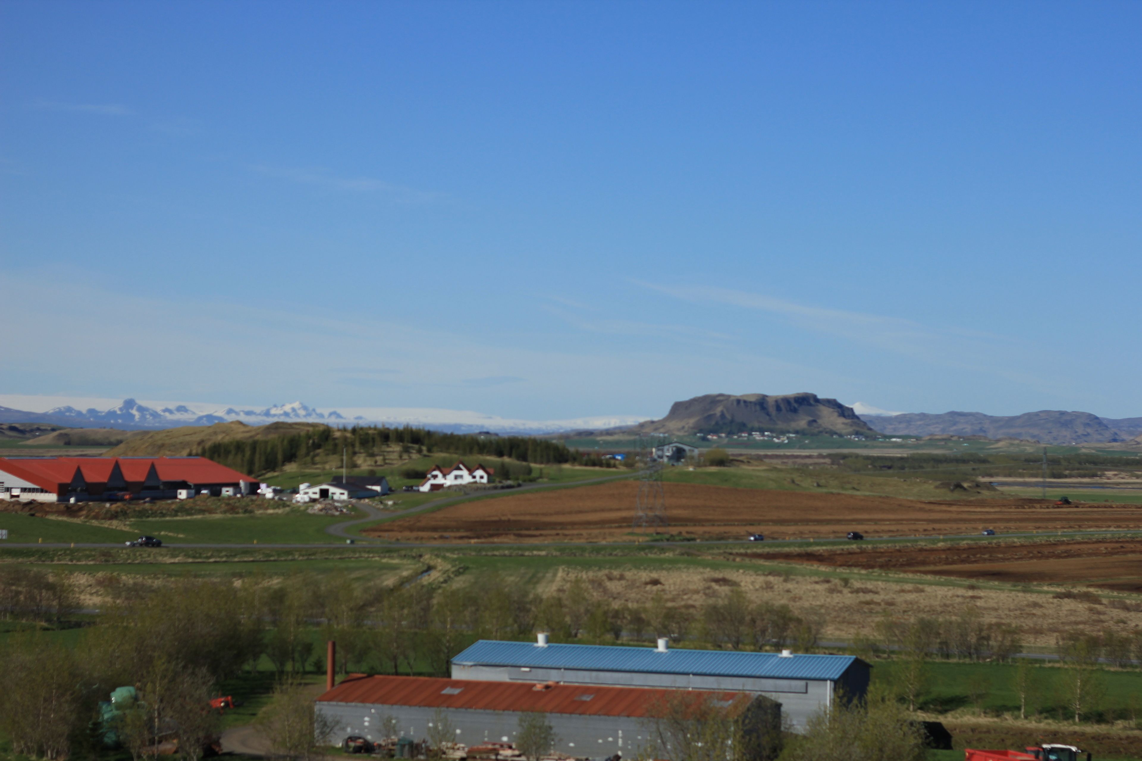 A rural landscape with buildings, fields, and mountains.