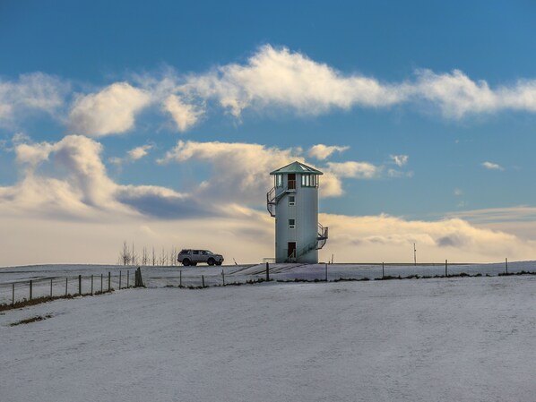 Un paisaje cubierto de nieve con una pequeña estructura tipo torre, una valla y un vehículo.