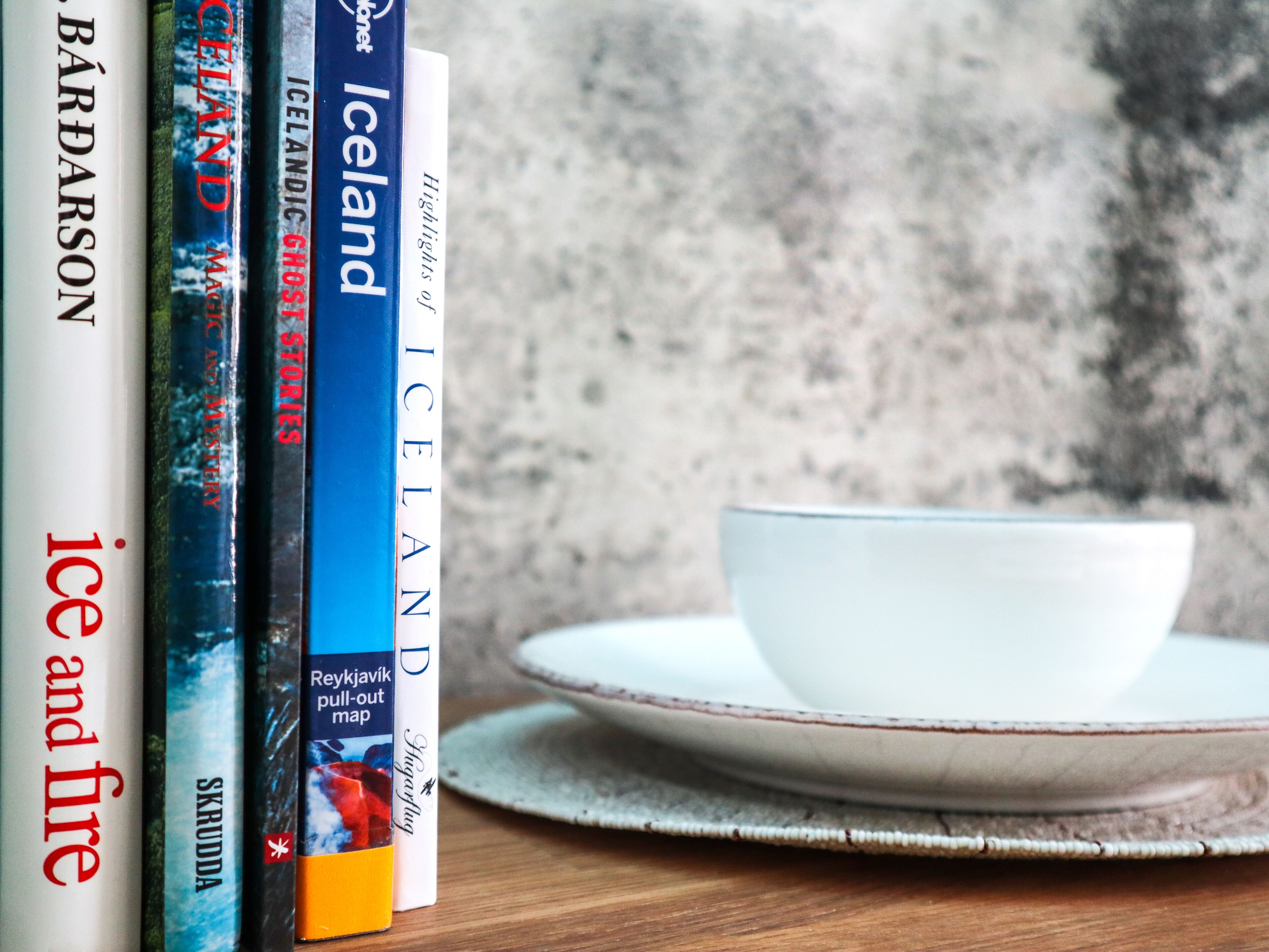 A row of books on a shelf with a bowl and plate on a table.
