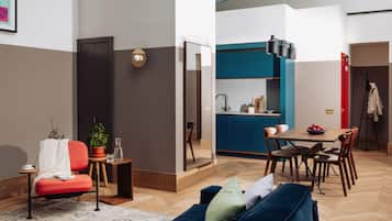 A modern living room with a sofa, a dining table with chairs, a kitchen area, and a large mirror.